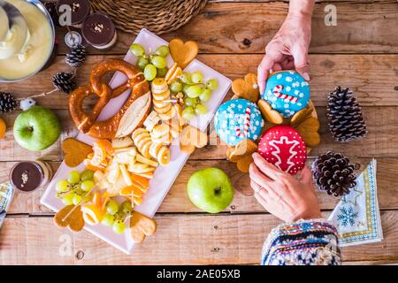 Couple de mains en vue supérieure, en tenant deux gâteaux sucrés de Noël sur une table en bois avec des fruits et des décorations d'hiver - home party avec la famille et les amis Banque D'Images