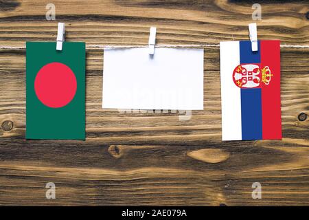 Drapeaux suspendus du Bangladesh et la Serbie attaché à corde avec pinces à linge avec de l'espace de copie sur papier blanc sur fond de bois.rapport diplomatique Banque D'Images