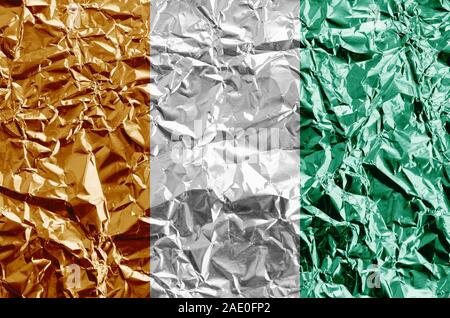 Côte d'Ivoire drapeau représenté dans des couleurs de peinture sur aluminium froissé brillant close up. Bannière sur fond rugueux texturé Banque D'Images