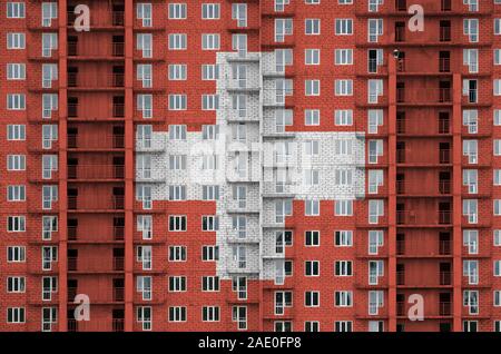 Drapeau suisse représenté dans la peinture de couleurs sur plusieurs étages du bâtiment résidentiel en construction. Bannière texturé sur grand fond mur de brique Banque D'Images