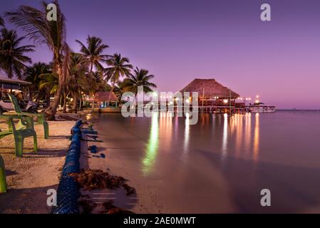 Un magnifiquement éclairé jusqu'au toit de chaume sur pilotis bungalow pendant le coucher du soleil dans l'île d'Ambergris Caye, Belize. Une longue exposition de droit. Banque D'Images