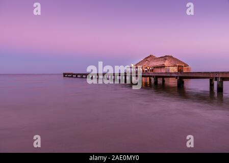 Un magnifiquement éclairé jusqu'au toit de chaume sur pilotis bungalow pendant le coucher du soleil dans l'île d'Ambergris Caye, Belize. Une longue exposition de droit. Banque D'Images