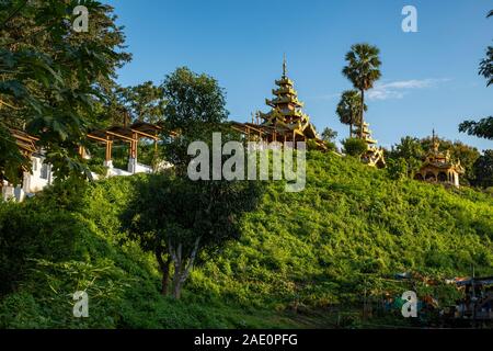 Un temple bouddhiste perché au sommet d'une colline d'arbres remplis et face à une série de petits temples dans un village le long de la rivière Chindwin, Myanmar Banque D'Images