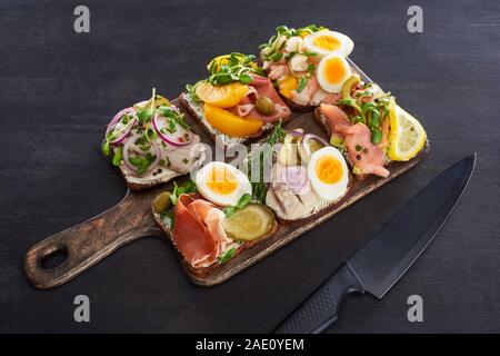 Planche à découper en bois avec couteau smorrebrod danois près de sandwichs sur surface grise Banque D'Images