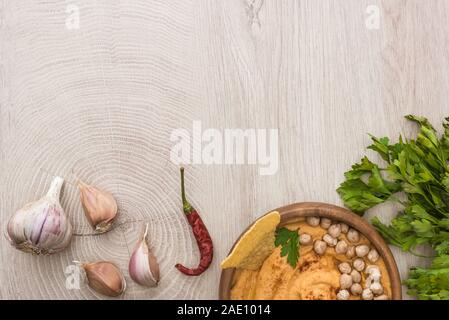 Vue de dessus de l'hummus délicieux avec les pois chiches, nacho dans un bol près de épices et le persil sur table en bois beige Banque D'Images