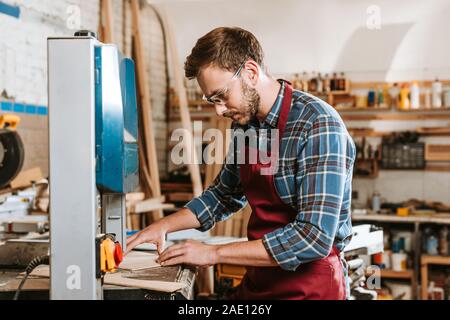 Focus sélectif de Carpenter en lunettes de sécurité et un tablier à l'aide de machine CNC Banque D'Images