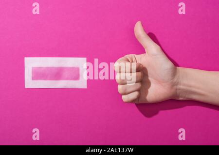 Portrait of woman showing thumb up près de cire épilation bande sur fond rose Banque D'Images