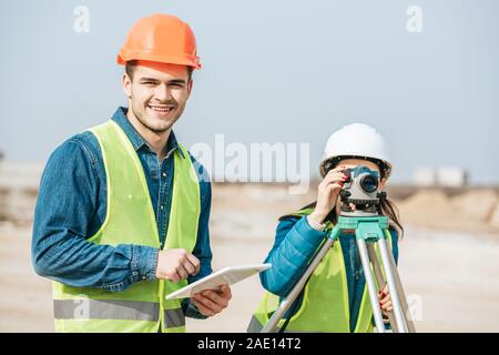 Smiling surveyor with digital tablet et collègue à la mesure de niveau Banque D'Images