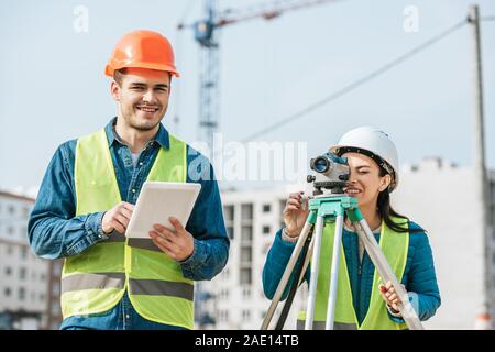 Les arpenteurs Smiling with digital tablet et la mesure de niveau sur site de construction Banque D'Images