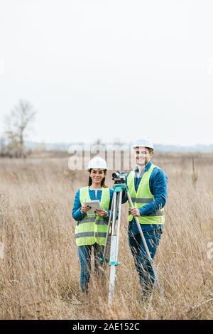 Les géomètres avec niveau numérique et tablette smiling at camera in field Banque D'Images