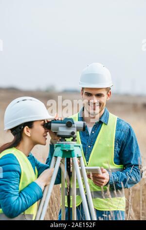 Travailler avec les arpenteurs souriant niveau numérique et tablette dans le champ Banque D'Images