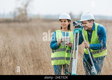 Smiling géomètres avec niveau numérique et tablette dans le champ Banque D'Images