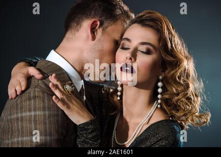 Belle femme aux yeux clos hugging homme dangereux sur noir Banque D'Images