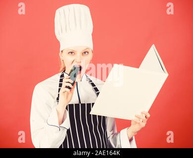 Faim. menu du restaurant. Suivre un régime culinaire. Femme au foyer avec. Livre de cuisine chef professionnel dans la cuisine manger du concombre. Cuisine. Femme au chapeau et un tablier cook. happy woman la cuisson des aliments sains par recette. Banque D'Images