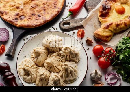 Vue de dessus de délicieux khinkali et khachapuri près de légumes et épices sur table de marbre Banque D'Images