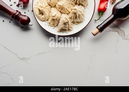 Vue de dessus de délicieux khinkali près de bouteille de vin, de légumes et d'épices sur table de marbre Banque D'Images