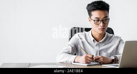 Vue panoramique shot of asian seo manager holding pencil and looking at laptop au cours webinaire Banque D'Images