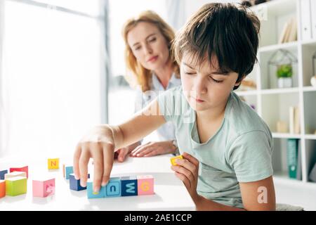 Portrait d'enfant dyslexique jouant avec des éléments constitutifs et au psychologue de l'enfant à l'arrière-plan Banque D'Images