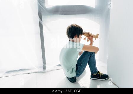 Portrait de l'enfant dyslexique assis sur le plancher en bois et jouer avec avion Banque D'Images