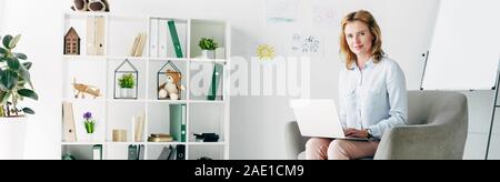 Vue panoramique tourné de psychologue pour enfants attrayant en shirt holding laptop et assis sur un fauteuil Banque D'Images