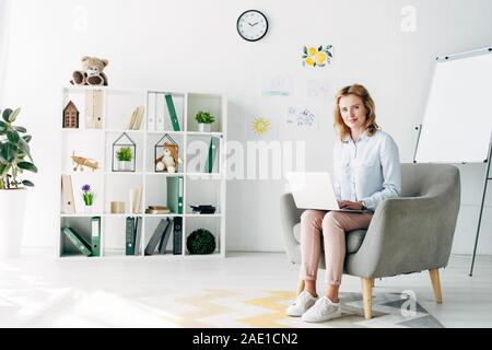 Psychologue pour enfants attrayant en shirt holding laptop et assis sur un fauteuil Banque D'Images