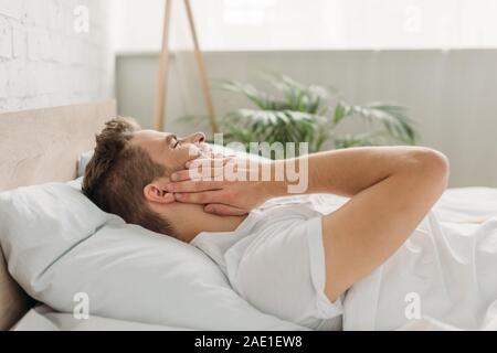 Jeune homme touchant joue en position couchée au lit et souffrant de maux Banque D'Images