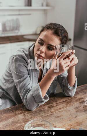 Femme tenant à côté du verre de whisky sur la table cendrier dans la cuisine Banque D'Images