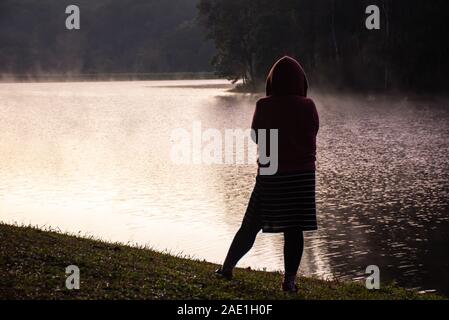 L'image derrière femme debout sur la pelouse et de la brume flottant au-dessus de l'eau au réservoir de Pang Tong à Mae Hong Son, Thaïlande. Banque D'Images