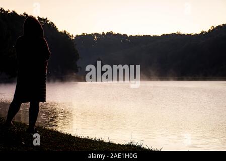 L'image derrière femme debout sur la pelouse et de la brume flottant au-dessus de l'eau au réservoir de Pang Tong à Mae Hong Son, Thaïlande. Banque D'Images