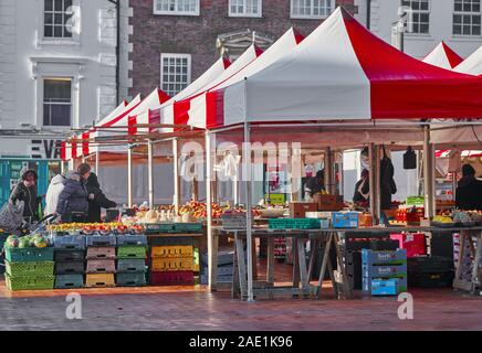 Les consommateurs à l'open-air jardiniers les étals de marché vente de fruits à la place du marché à Northampton, en Angleterre, par une froide journée d'hiver ensoleillée. Banque D'Images