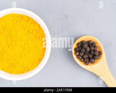 Le curcuma dans un bol blanc et le poivre noir dans une cuillère de bois sur un fond de béton gris. Concept de saine alimentation Banque D'Images