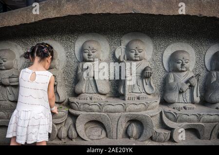 Chengdu, Chine - Juillet 2019 : Petite fille chinoise dans une robe blanche laissant fleurs sous les petites sculptures en saint monastère de Wenshu Banque D'Images