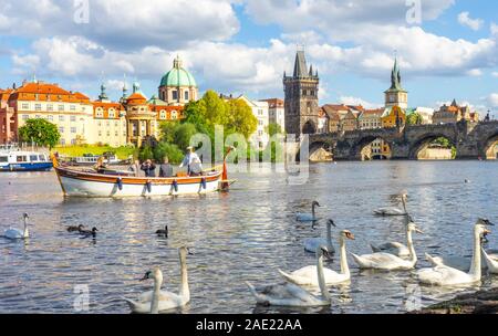 Petit bateau en bois avec les touristes des visites et des croisières sur la rivière Vltava cygnes blancs Charles Bridge Prague République tchèque. Banque D'Images