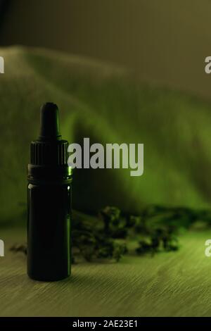 Seul 10 ml flacon en verre noir entouré d'herbes séchées sur la table en bois blanc avec rétro-éclairage vert Banque D'Images