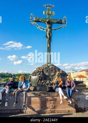 Les touristes assis sous la sculpture Crucifix et Calvaire avec texte hébraïque médiévale taunting citoyens juifs Charles Bridge Prague République tchèque. Banque D'Images