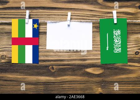 Drapeaux suspendus de République centrafricaine et de l'Arabie saoudite attache à corde avec pinces à linge avec de l'espace de copie sur papier blanc sur fond de bois Banque D'Images