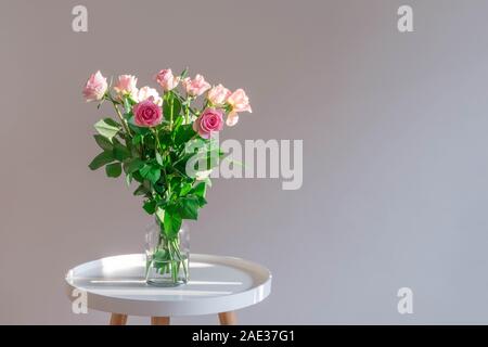 Des roses rose pastel vase en verre sur table de café blanc sur fond neutre. Banque D'Images