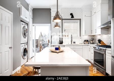 Une luxueuse cuisine blanche avec des appareils en acier inoxydable et planchers de bois de couleur claire. La vue montre une scène d'hiver. Banque D'Images