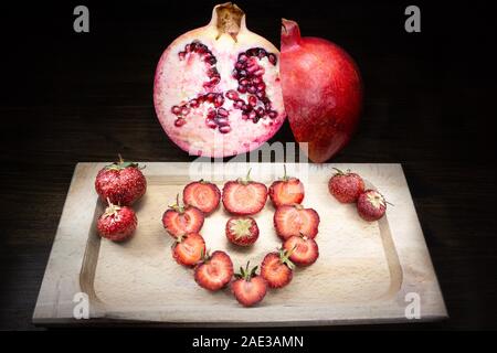 Une composition colorée et de coeur pour deux excellents fruits : fraises et de grenadiers, positionnée sur une vieille table et allumé à l'aide de peinture claire Banque D'Images