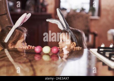 Regarde l'autre. Deux soeurs drôles en oreilles de lapin à l'un l'autre sur la table Banque D'Images