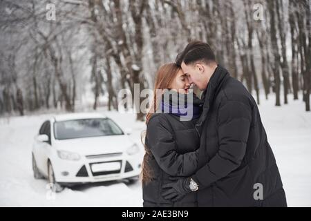 Sentiment de plaisir. Superbe jeune couple se place en avant de leur automobile blanc dans la forêt enneigée Banque D'Images