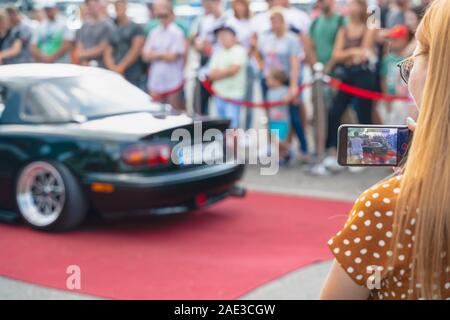 Prenez une photo de fille jolie nouveau véhicule par son téléphone mobile. L'analyse de visiteur voiture moderne à Kiev, Ukraine. Image horizontale Banque D'Images