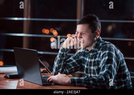 Brun court. L'homme à la chemise à carreaux ont des travaux supplémentaires à la nuit dans le bureau Banque D'Images