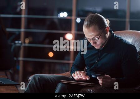 L'homme aux cheveux longs. Classy businessman dans eyewear travaille seul dans le bureau de la nuit, Banque D'Images