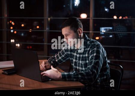 Travaillant depuis si longtemps donne de l'argent supplémentaire. L'homme à la chemise à carreaux ont des emplois supplémentaires à la nuit dans le bureau Banque D'Images