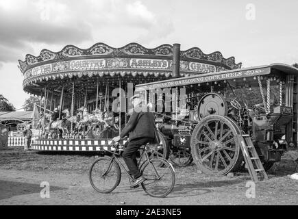 Vieil homme qui fait du vélo et du vélo dans un parc d'expositions traditionnel à vapeur vintage avec un rond-point de l'excitation et un moteur de traction Malpas Angleterre Banque D'Images