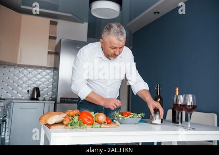 Prendre un peu de sel. L'homme en chemise blanche à la préparation de la nourriture sur la cuisine en utilisant des légumes Banque D'Images