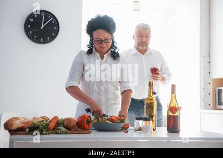 Tente pour son mari. L'homme et sa femme en chemise blanche à la préparation de la nourriture sur la cuisine en utilisant des légumes Banque D'Images