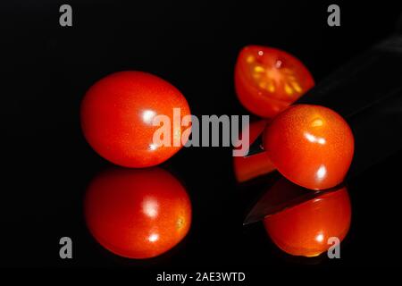 Tomates Raisins contre un fond noir étant en tranches avec un couteau bien aiguisé sur une surface réfléchissante. Les couleurs vibrantes et prix pour l'exemplaire Banque D'Images