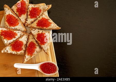Spoon et la plaque de pain noir avec du caviar rouge foncé sur fond de table avec l'exemplaire de l'espace. Caviar rouge des sandwichs. Alimentation saine. Banque D'Images